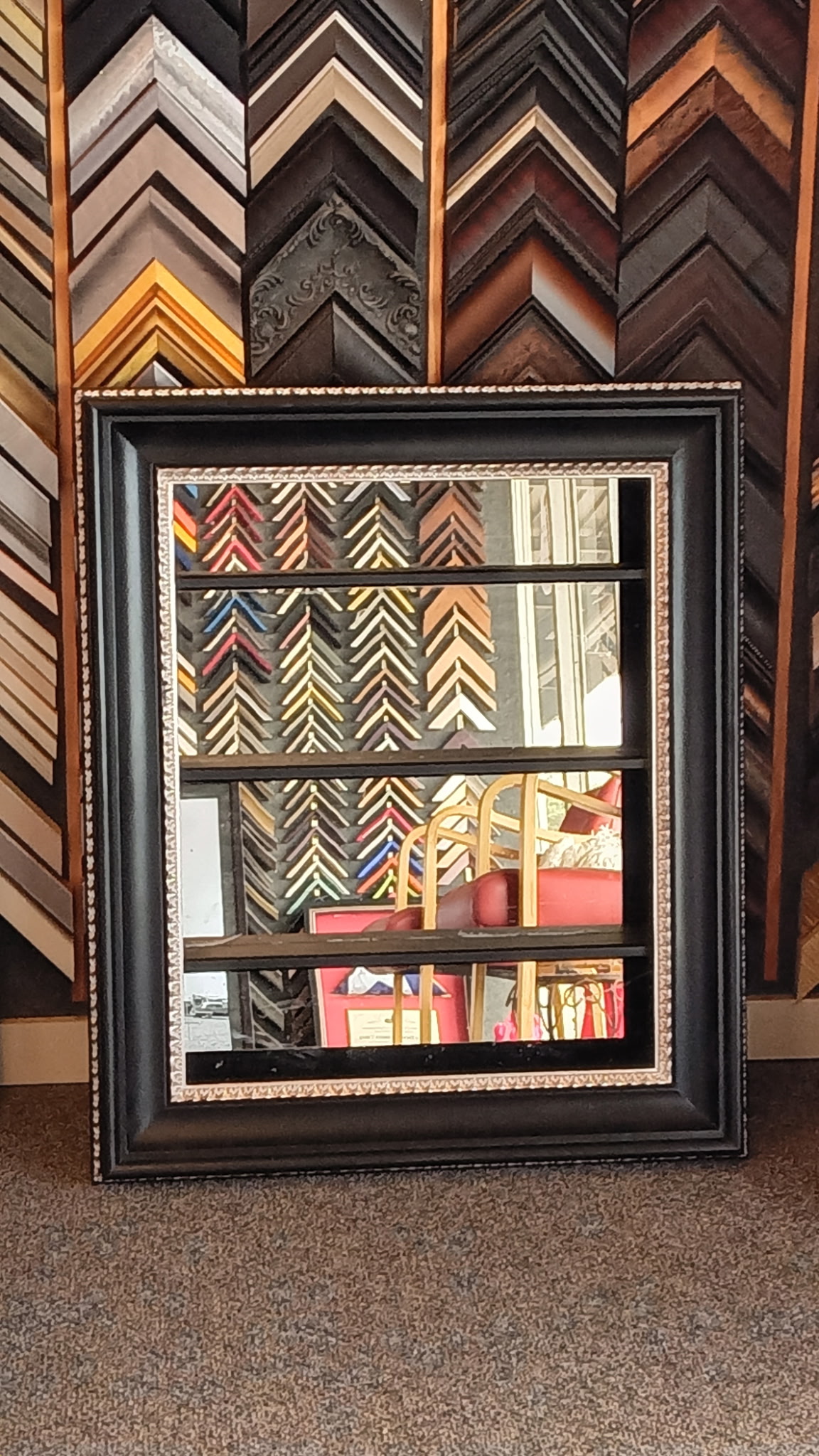 Large black-framed mirror with silver beaded edges leaning against the moulding wall