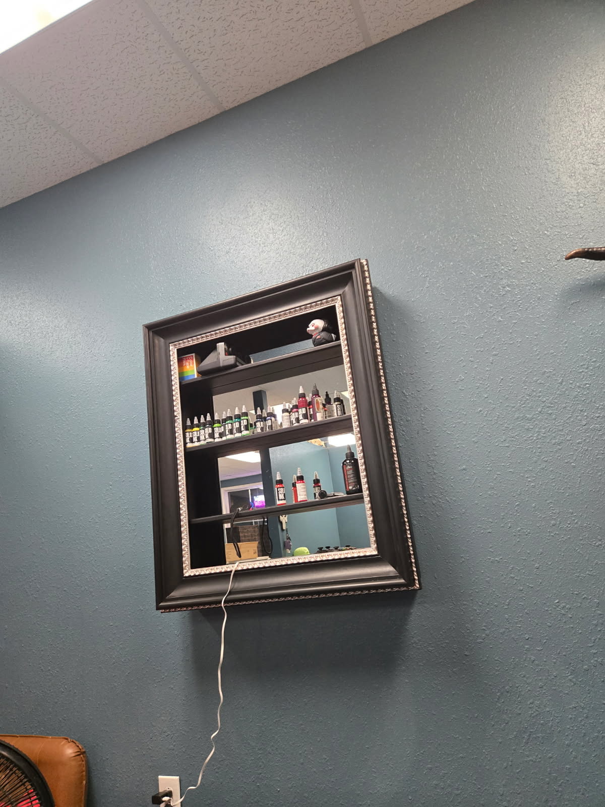 Wall-mounted framed display case with mirrored back and shelves of tattoo ink bottles