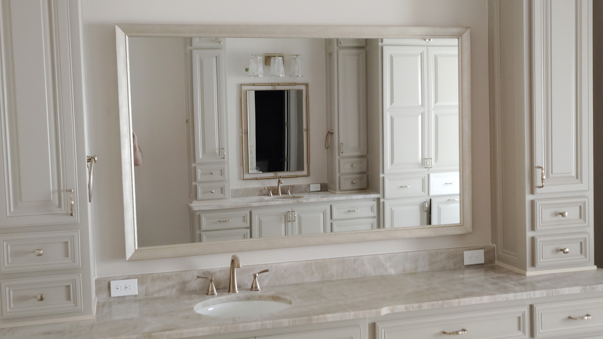 Champagne-framed bathroom vanity mirror between custom cabinets