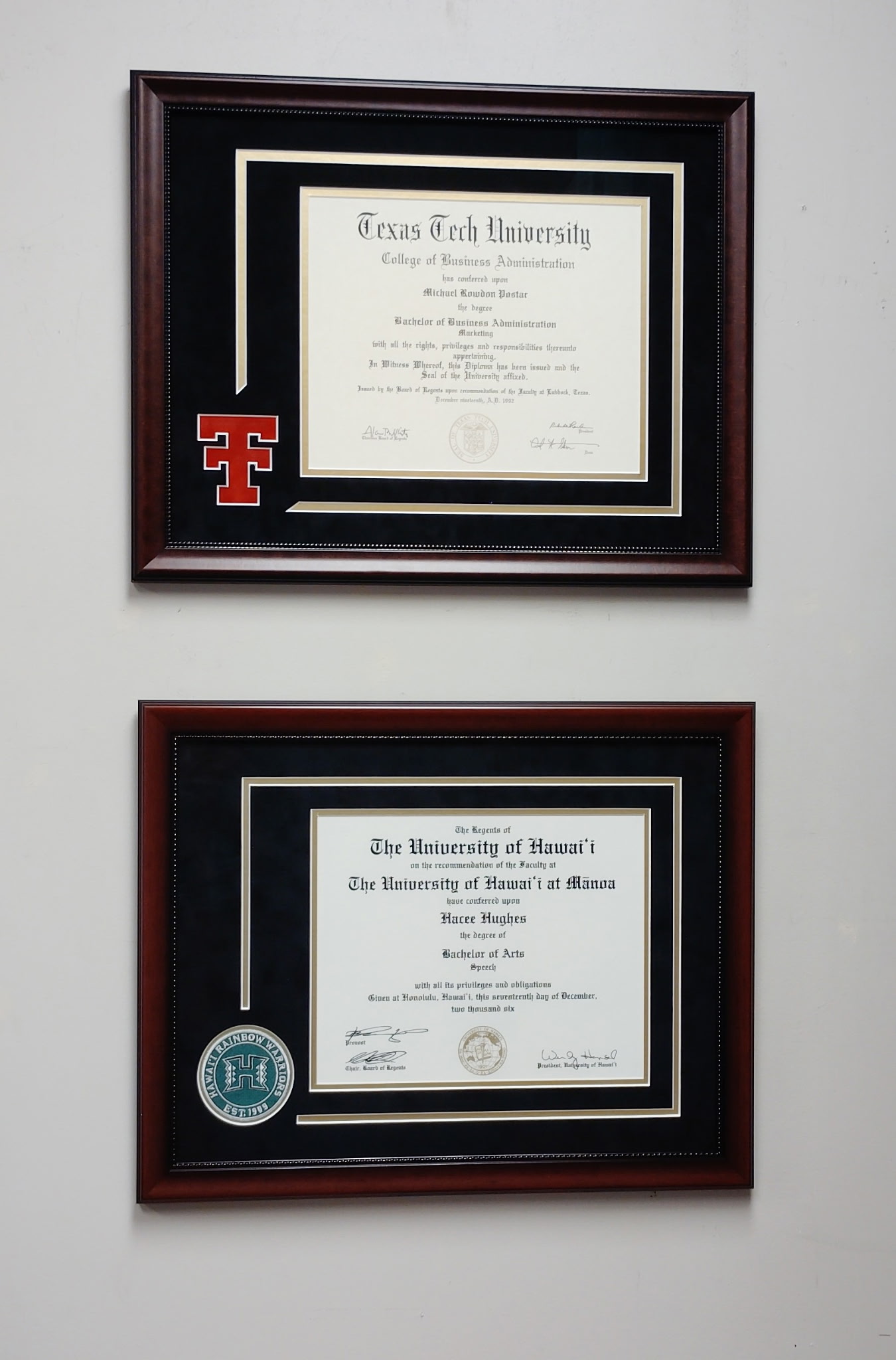 Two diplomas in matching dark-wood frames with black mats and university emblems